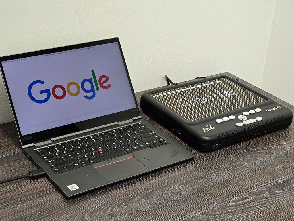 Picture of a Laptop and a connected graphic Braille Display showing the Google website